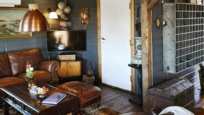Un salon avec un canapé en cuir marron, une table basse sur laquelle se trouvent un livre et des fleurs, un téléviseur et une porte en bois rustique.