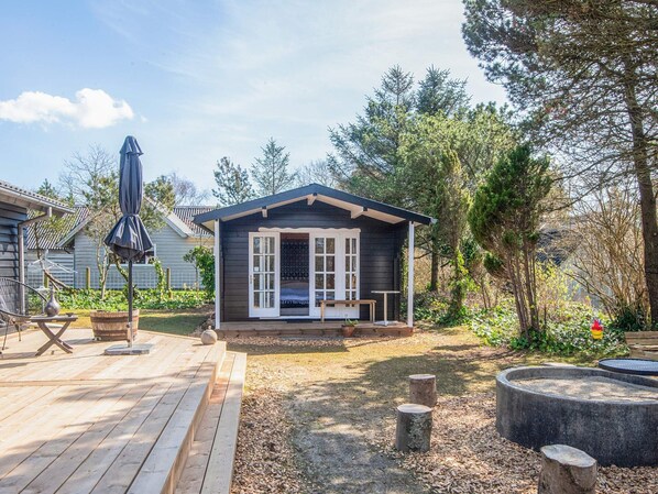 A small cabin with a deck, a grill outside, and a fire pit in the yard.