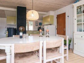 Un comedor con una mesa redonda, sillas, una lámpara colgante y una cocina al fondo.