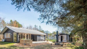 A cabin with a large porch, a small attached structure, and a surrounding wooded area. - 6 Person Holiday Home in Hemmet (Hemmet)