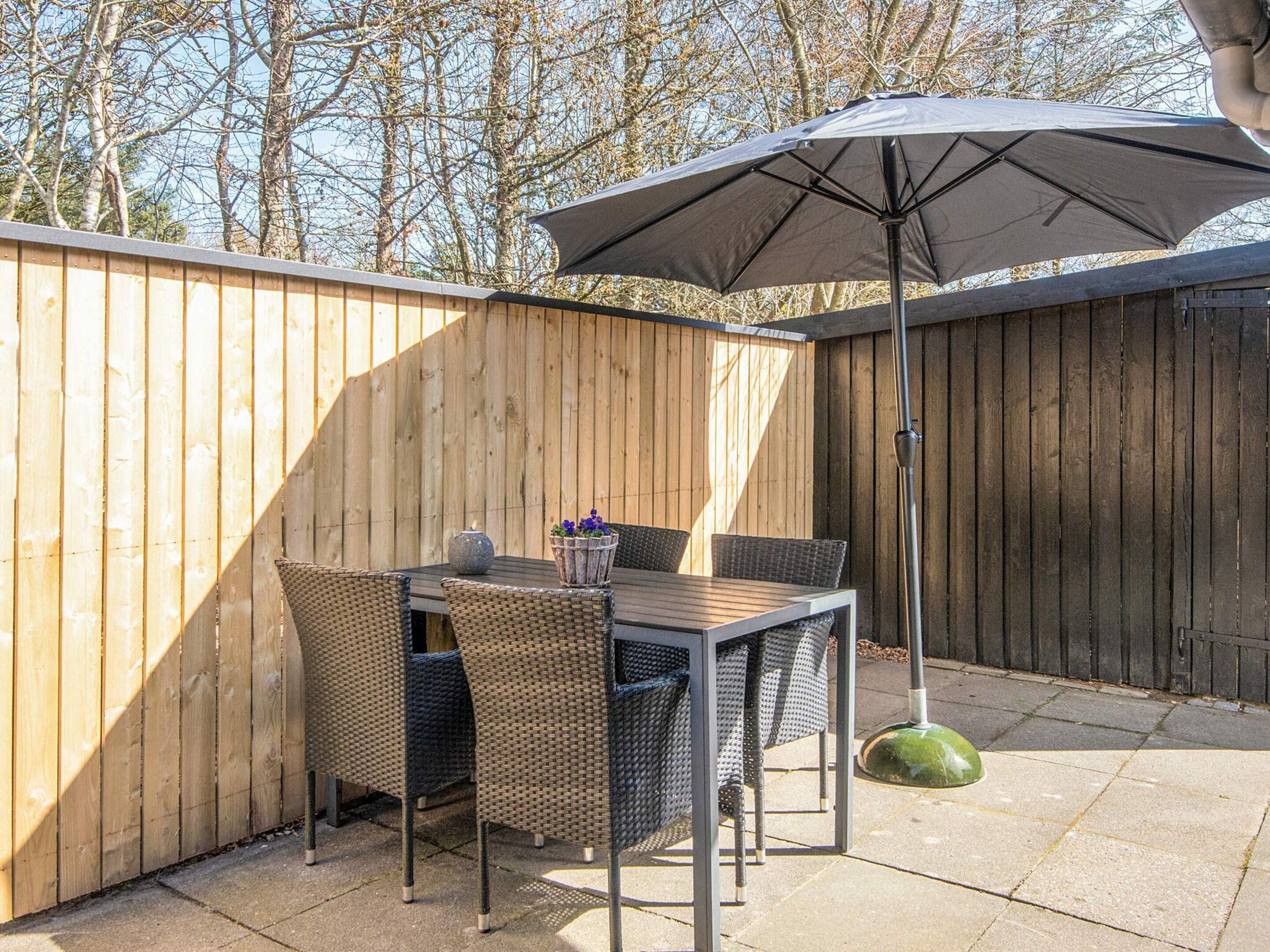 A patio with a table and chairs, an umbrella, and a wooden fence.
