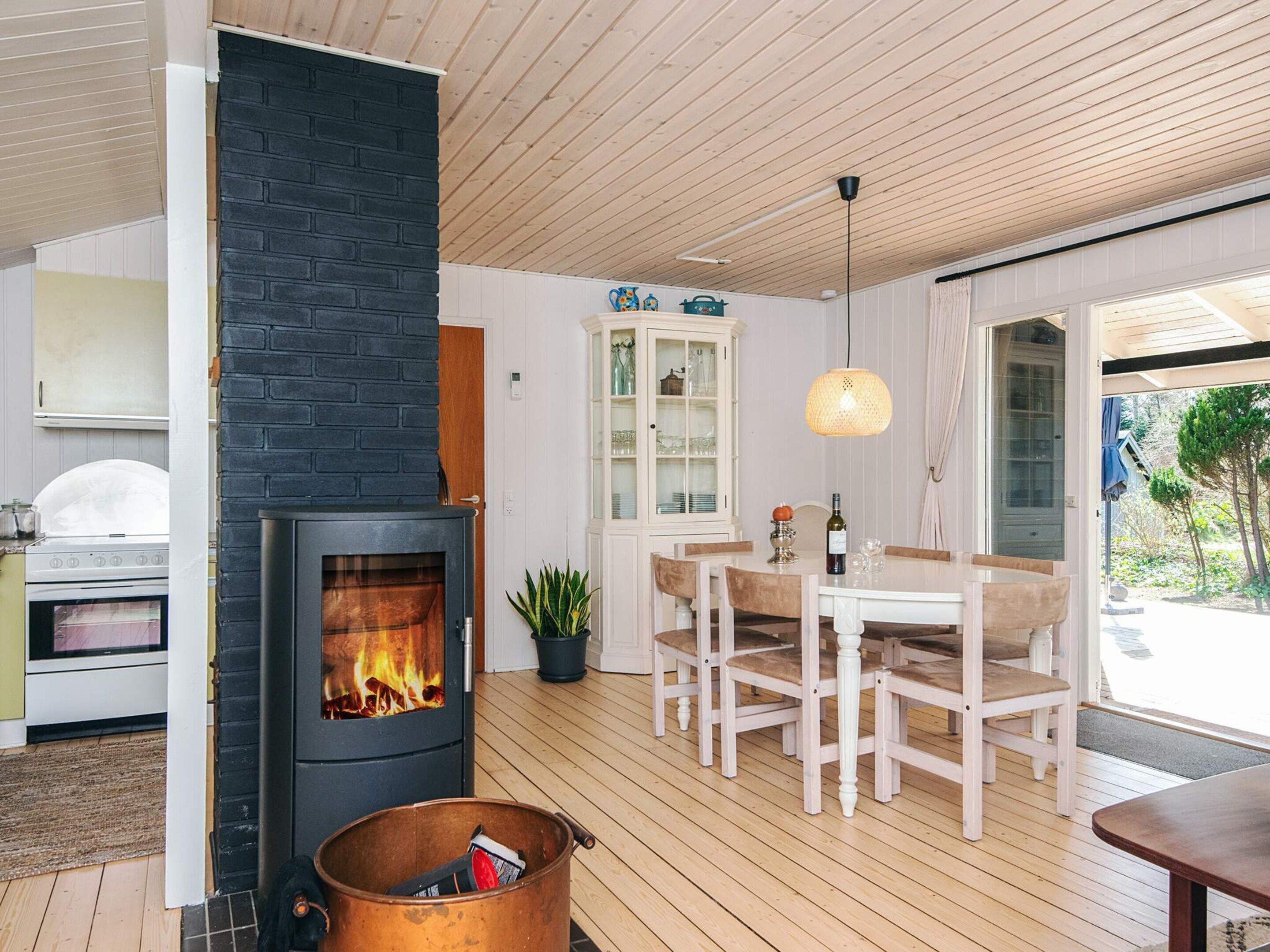 A modern kitchen with a wood-burning stove, a dining area with a table and chairs, and a large window.