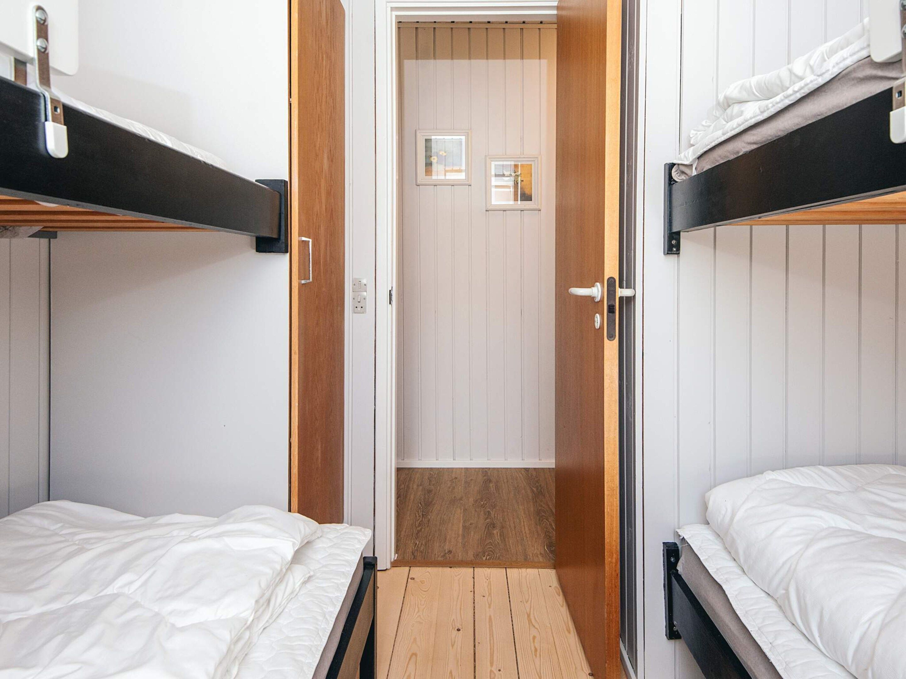 Une pièce avec des lits superposés, un plancher en bois et une porte donnant sur une autre pièce.