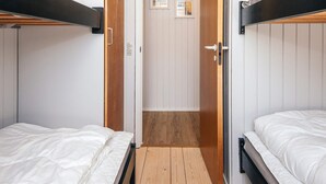 A room with bunk beds, a wooden floor, and a door leading to another room.