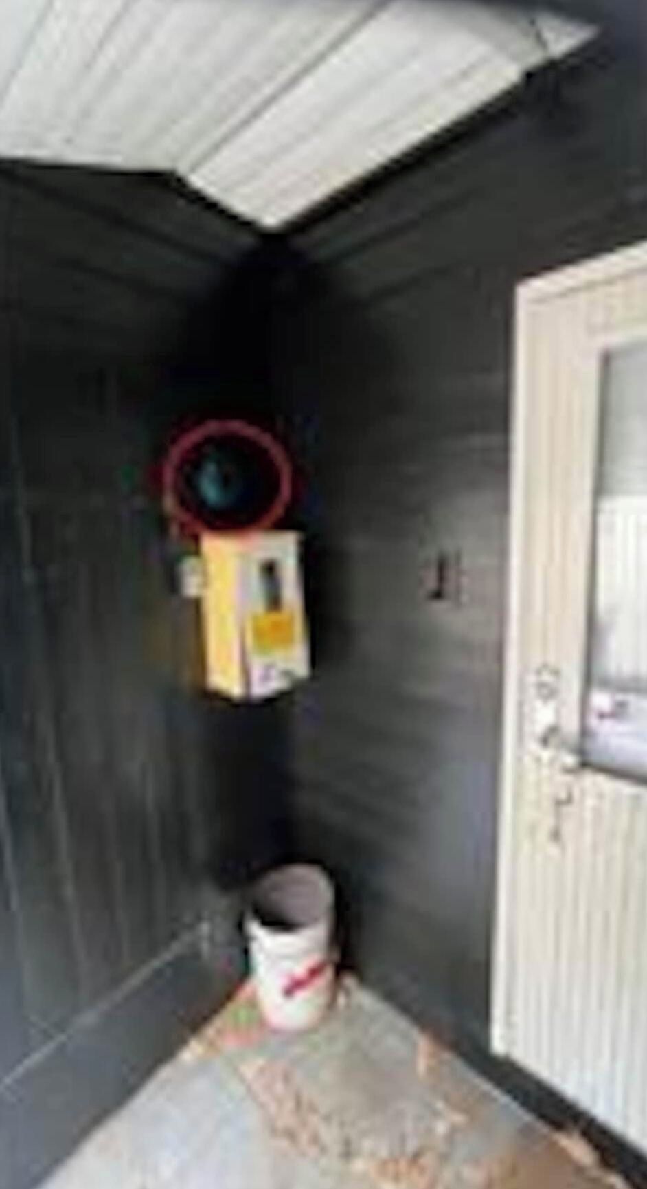 A room with a door, a window, a white bucket, and a yellow object on the wall.
