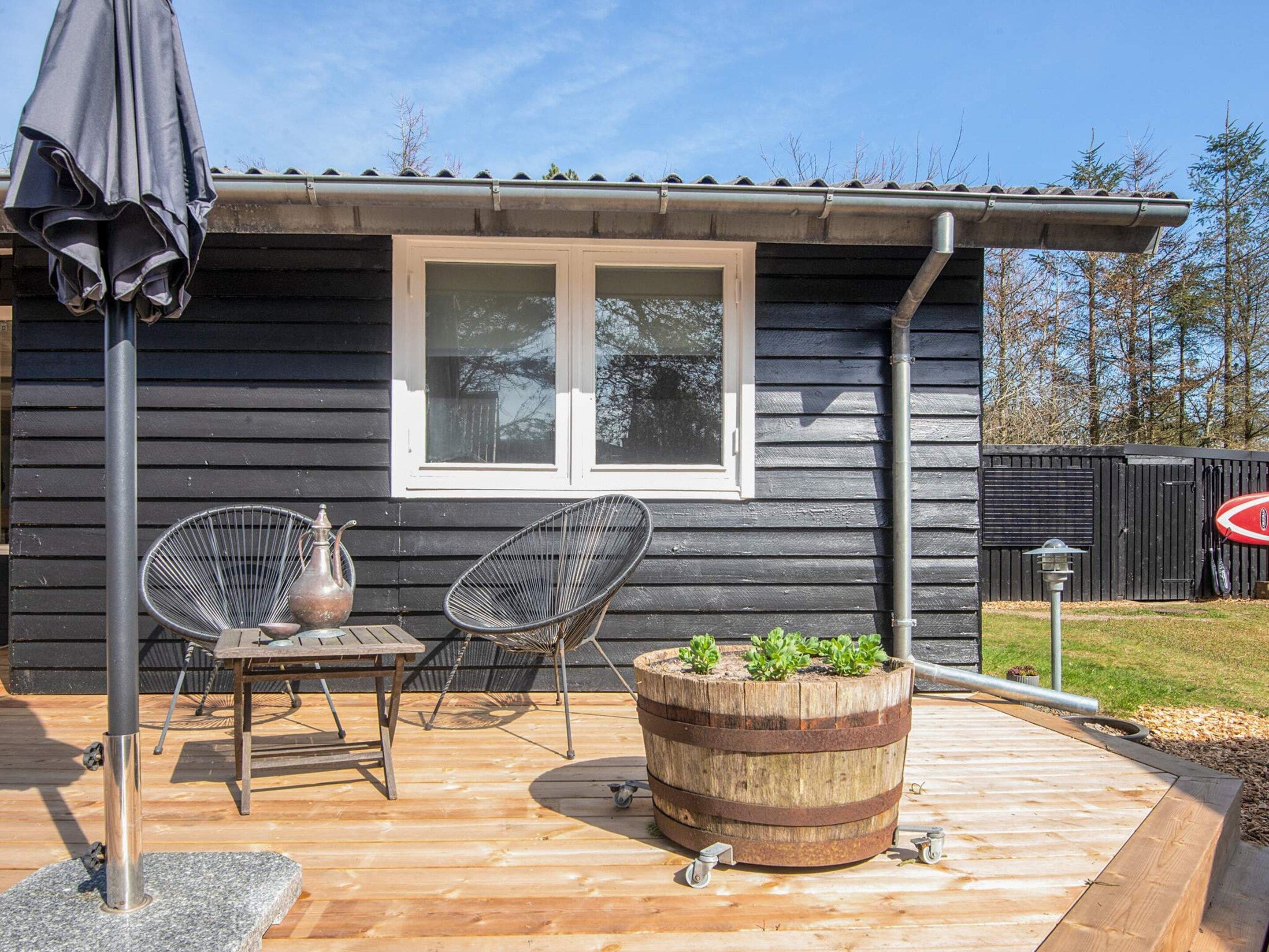 A wooden deck with a metal table, two chairs, a potted plant, and a barrel planter.
