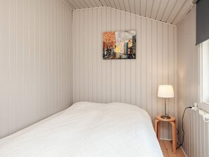 A single-bed room with a white bedspread, a small wooden stool, a floor lamp, and a cityscape painting on the wall. - 6 Person Holiday Home in Hemmet (Hemmet)