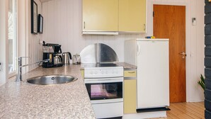 A kitchen with a granite countertop, stainless steel sink, white and yellow cabinets, a white refrigerator, and a wooden door.