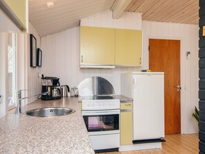 Una cocina con encimera de granito, pileta de acero inoxidable, muebles de color blanco y amarillo, un refrigerador blanco y una puerta de madera.