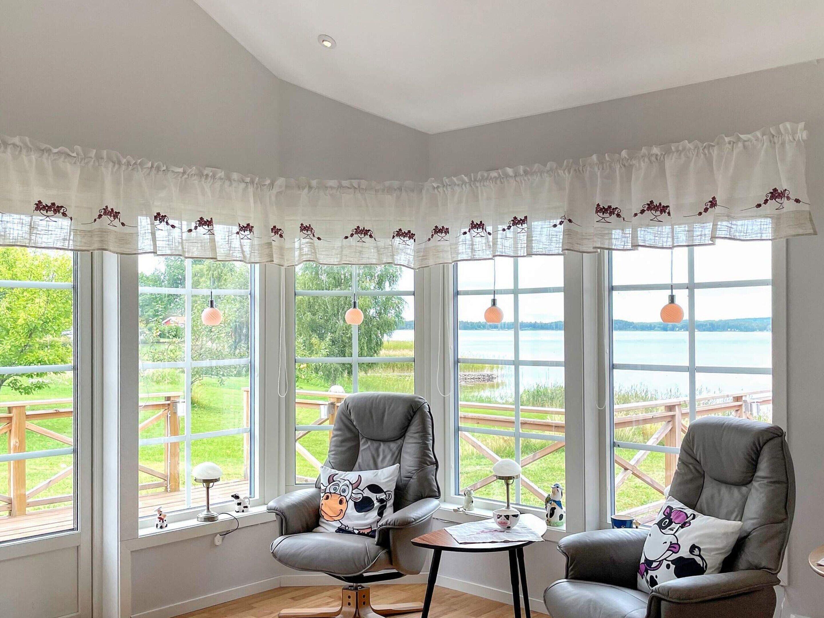 A room with two leather chairs, a small table, and large windows with white curtains.
