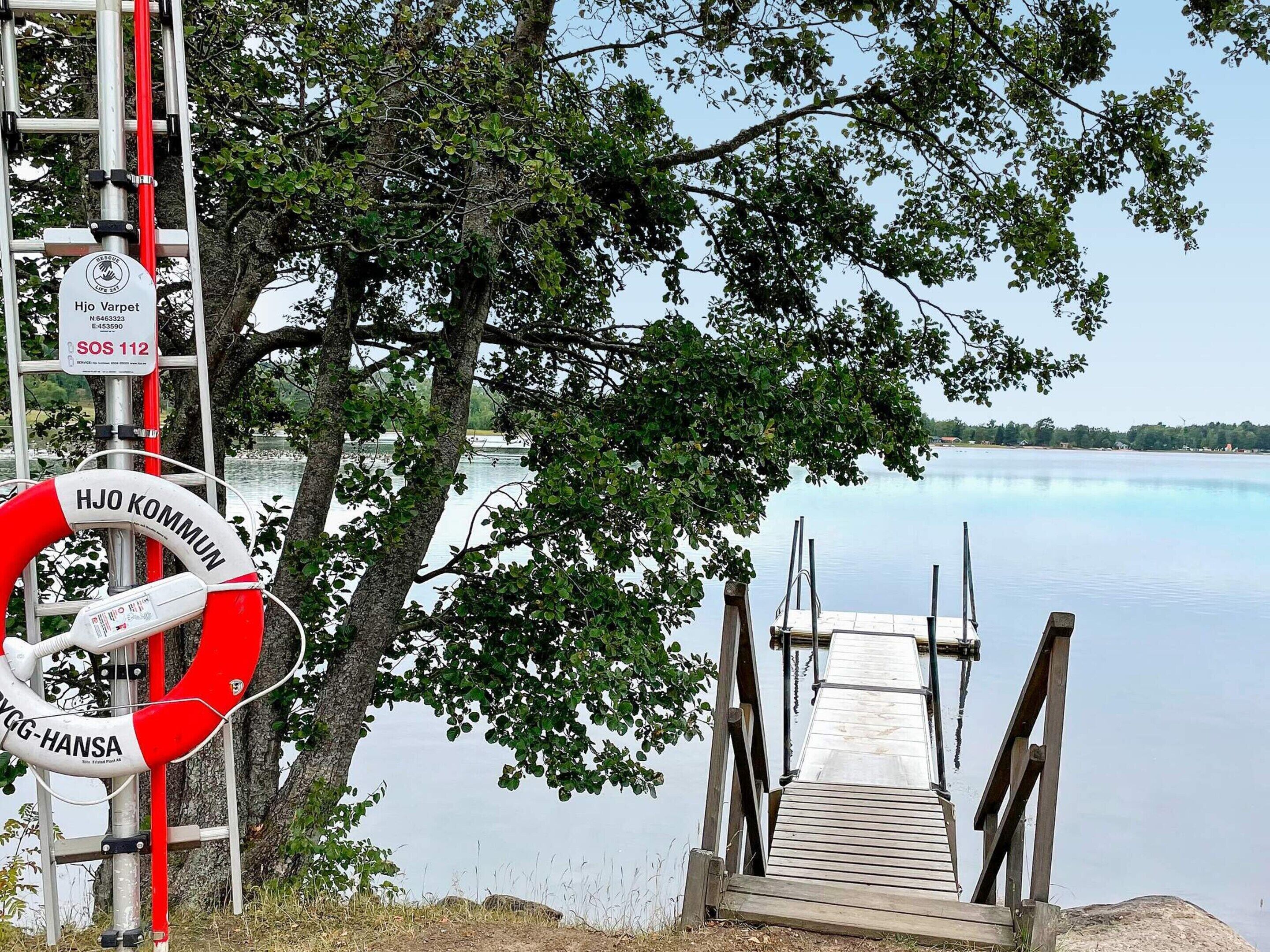A lifebuoy, a wooden dock, and a calm lake with trees in the background.