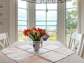 A dining table with a white tablecloth, a vase with flowers, and a view of a lake through large windows. - 4 Star Holiday Home in Hjo (Hjo)