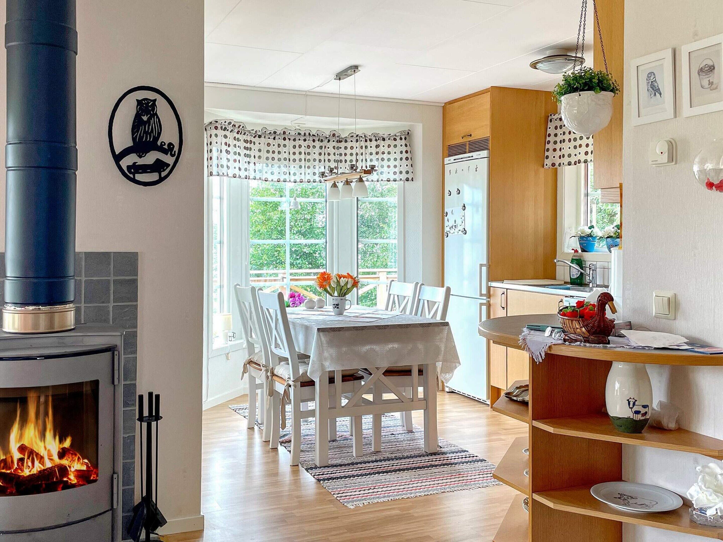 Un rincón comedor acogedor con chimenea, sillas blancas, una mesa con flores y vistas a zonas verdes.