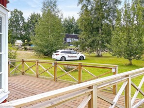 En vit bil parkerad på ett trädäck med utsikt över ett hus och träd i bakgrunden.