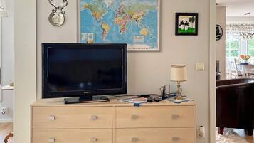 A room with a large flat-screen TV on a wooden dresser, a world map, a framed picture of a giraffe, and a lamp.
