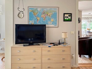 Une pièce avec une grande télévision à écran plat posée sur une commode en bois, une carte du monde, un tableau encadré représentant une girafe et une lampe.