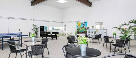 A spacious indoor area with a pool table, multiple seating arrangements, and a variety of plants.