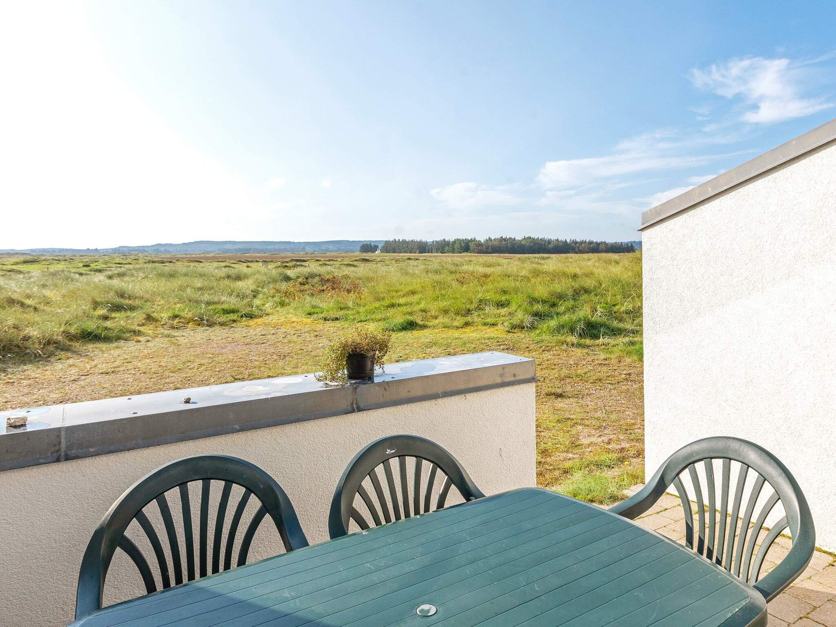 Un patio con una mesa y sillas, con vista a un campo cubierto de césped.