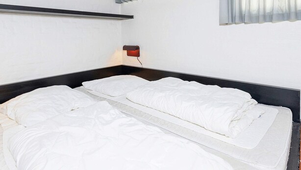 A single bed with a headboard, a bedside table with a lamp, and a window with blinds.