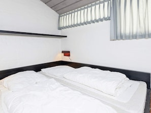 A single bed with a headboard, a bedside table with a lamp, and a window with blinds.