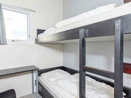Una cama litera con ropa blanca, una mesita pequeña y una ventana.