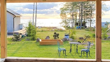 Una terraza de madera con vistas a un jardín césped, un banco de madera y una mesa de metal.
