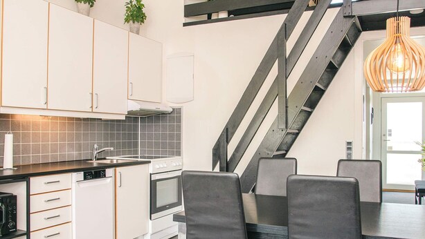 A modern kitchen with white cabinets, a built-in oven, and a dining area with black chairs. - 6 Person Holiday Home in Ringkobing (Ringkobing)