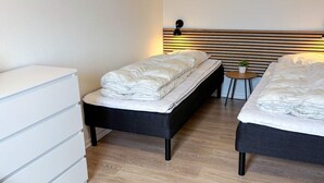 A hotel room with two beds, a bedside table, a small round table with a plant, and a white dresser. - 6 Person Holiday Home in Ringkobing (Ringkobing)