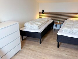 Quarto de hotel com duas camas, uma mesa de cabeceira, uma pequena mesa redonda com uma planta e uma cômoda branca.