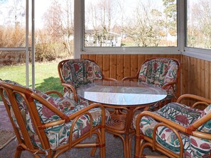 Una mesa redonda de cristal rodeada por cuatro sillas de mimbre con tapicería floral, frente a una pared de paneles de madera con vista a una zona residencial.