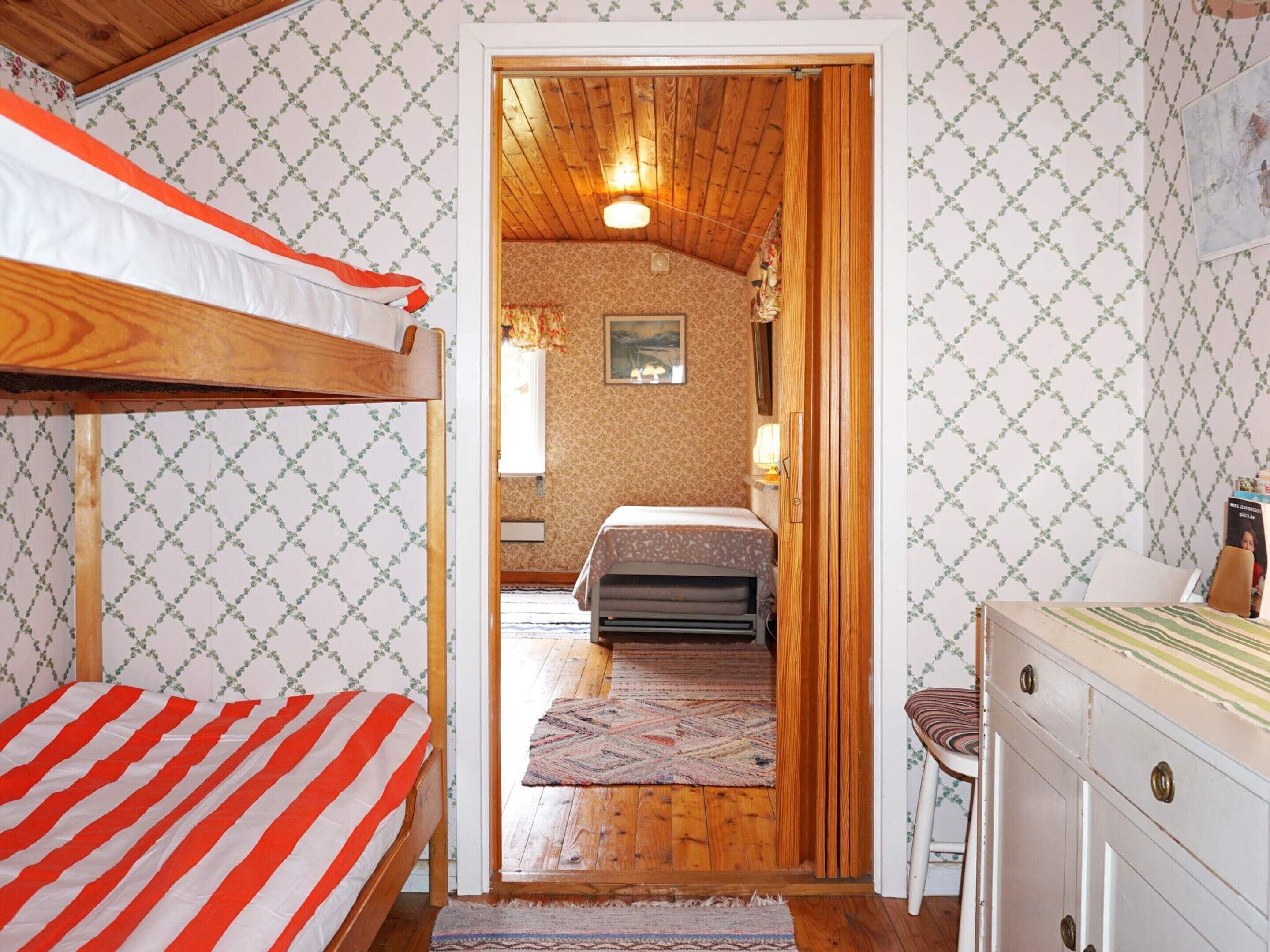 A room with a bunk bed, a wooden door leading to another room, and a desk with drawers.