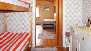 Une pièce avec un lit superposé, une porte en bois donnant sur une autre pièce et un bureau avec des tiroirs.