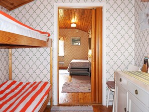 Una habitación con literas, una puerta de madera que da a otra habitación y un escritorio con cajones.