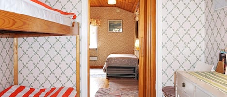 A room with a bunk bed, a wooden door leading to another room, and a desk with drawers.