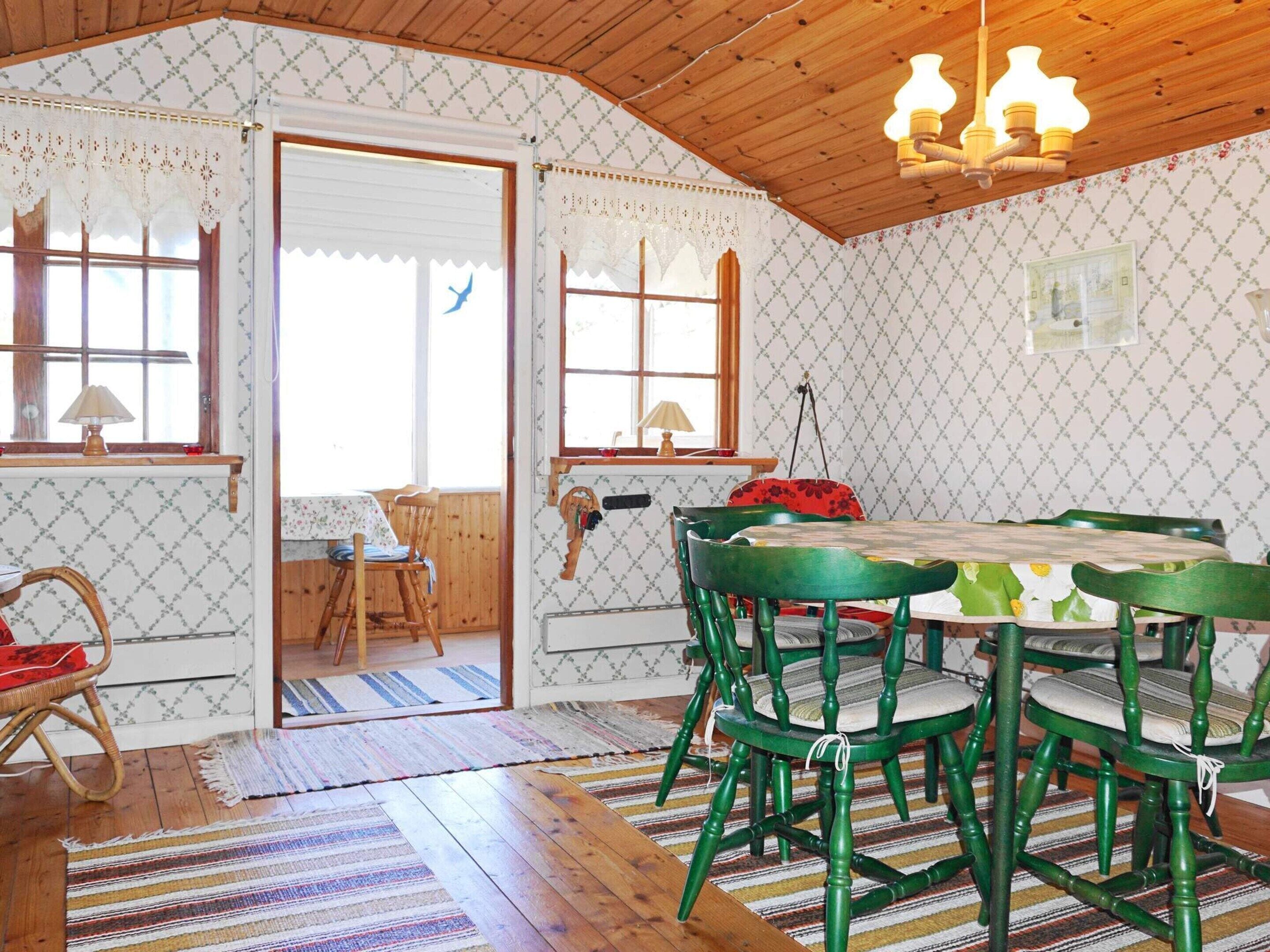 Een kamer met een houten plafond, behang met een patroon, een eettafel met stoelen en een deur die naar buiten leidt.