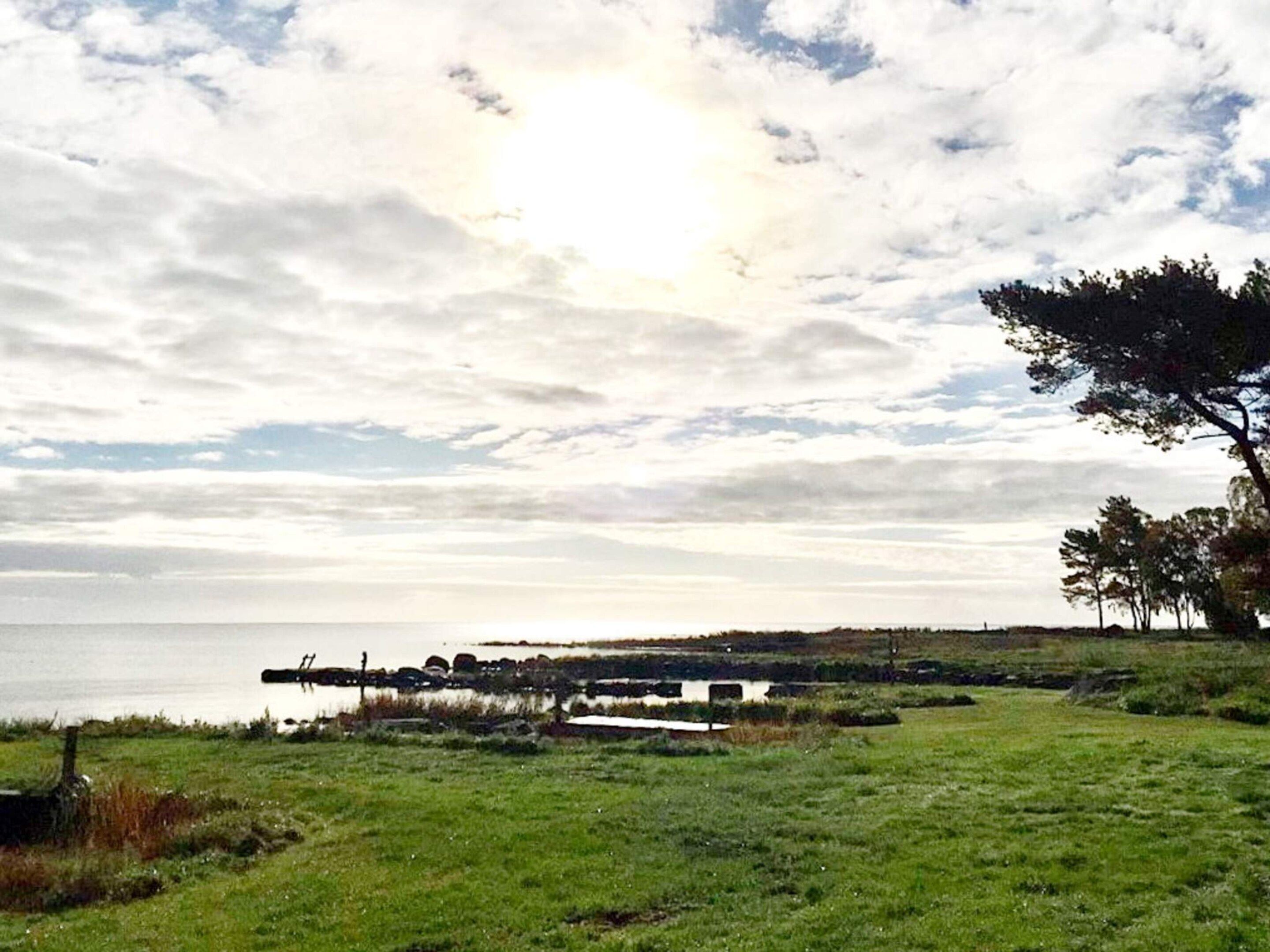 A grassy field with a body of water and a cloudy sky.