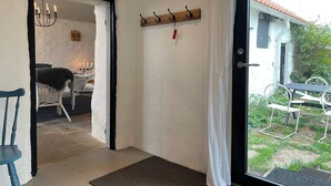 Une pièce comprenant une table à manger et des chaises, un lustre, un porte-manteau et donnant sur l’extérieur.