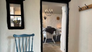 Une pièce avec une chaise bleue, un miroir et une porte qui donne sur une autre pièce, où se trouvent un lustre et une table.