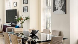 A modern dining area with a glass table, cushioned chairs, and a large painting on the wall.