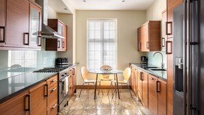 A modern kitchen with wooden cabinets, a gas stove, a stainless steel range hood, a glass dining table with chairs, and a refrigerator.