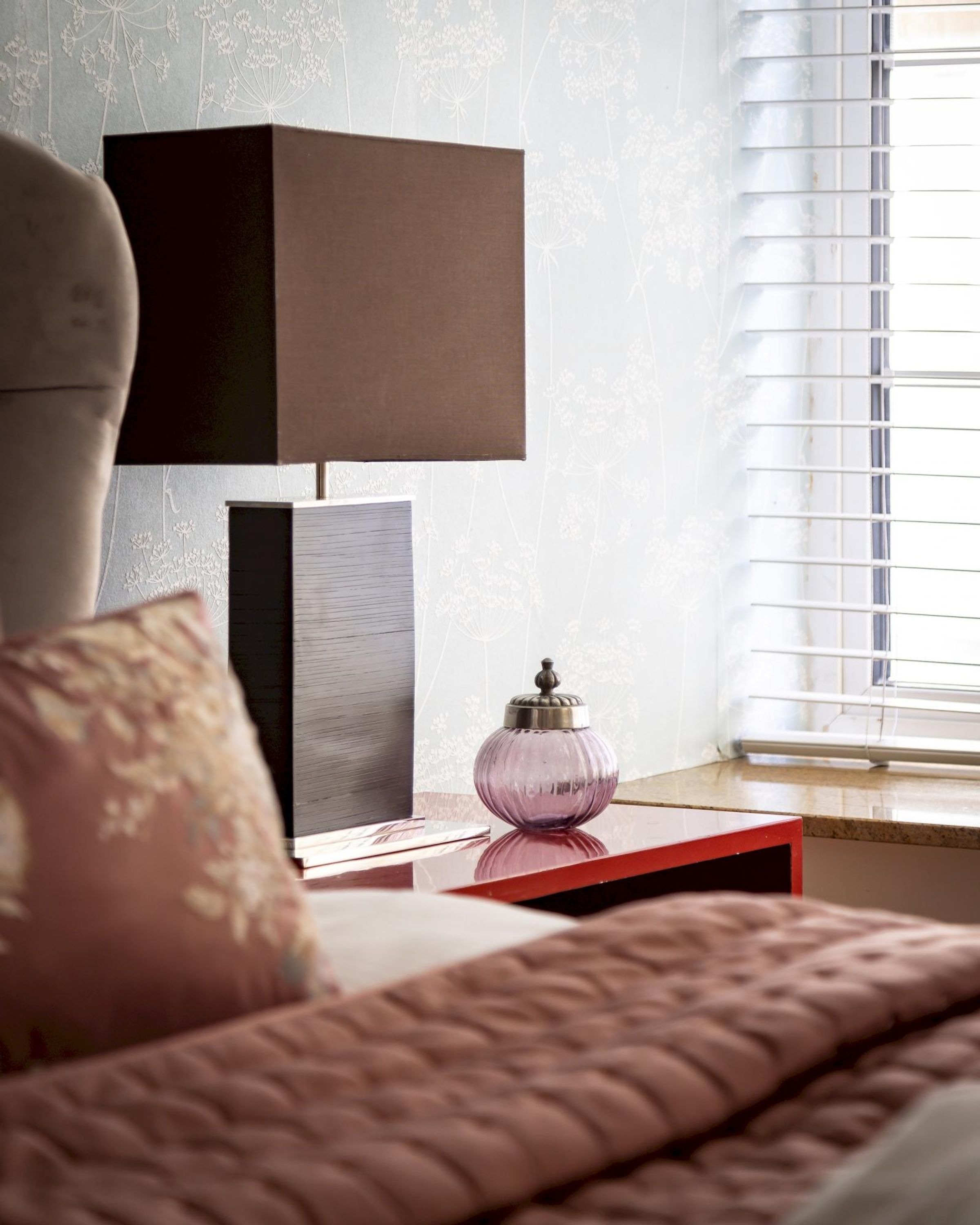 Une chambre à coucher avec un lit, une table de chevet, une lampe et une fenêtre avec des stores.