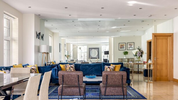 A spacious living room with a blue sofa, two armchairs, a dining table, and a large window.