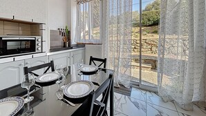 Un coin repas avec une table dressée pour quatre personnes, un four à micro-ondes et une vue sur l’extérieur grâce à de grandes fenêtres.