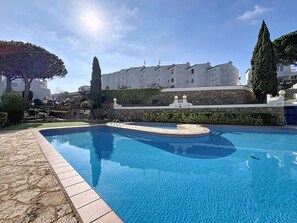 A swimming pool with a stone border, a stone wall, and a building in the background.
