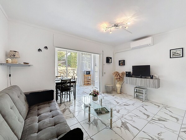 A modern living room with a grey sofa, a glass coffee table, and a TV on a wooden stand.