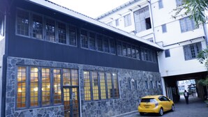 Un edificio de fachada de piedra, con amplias ventanas y un coche amarillo estacionado frente a él.