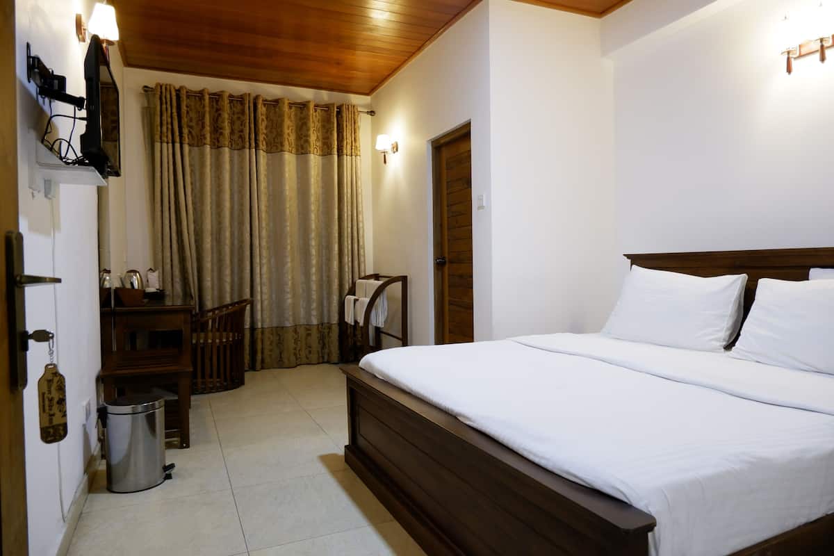 Una habitación de hotel con una cama de madera, un escritorio pequeño con lámpara, una silla, un cubo de basura y una puerta.