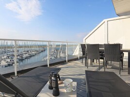 Una terraza con vistas a un puerto deportivo, amueblada con sillas, una mesa, unos binoculares y una taza.