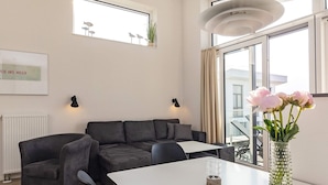 A modern living room with a sectional sofa, a dining table, and a vase of flowers.