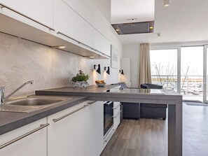 A modern kitchen with a central island, stainless steel appliances, and a view of the marina through large windows. - 5 Star Holiday Home in Wendtorf (Wendtorf)
